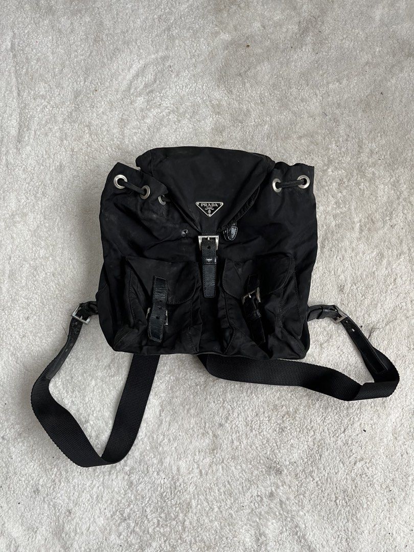 AUTHENTIC Prada Tessuto Nylon BackpackProject Bag (Category: Backpacks) located in General Trias. Submitted by zrchustle.604 (Listing ID 1462178129, Image 1). Description: Prada Tessuto Nylon Backpack, featuring the brand's iconic enameled triangle logo plaque, dual front buckle pockets, and a relaxed drawstring design. Check detailed pics sa issue. Originally debuting in the 1980s, this utilitarian luxury silhouette remains one of Prada's most s