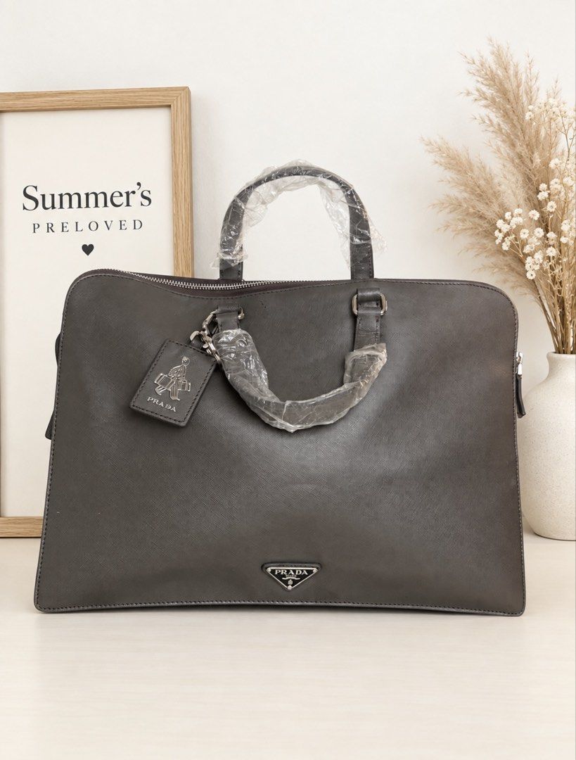 Pradudung Saffiano Leather Briefcase (Category: Laptop Bags & Sleeves) located in Taguig. Submitted by summers.preloved (Listing ID 1462232179, Image 2). Description: 👜 Bag Features 💜 Signature Saffiano crosshatch leather 🩶 Dark charcoal/graphite colour 💼 Structured briefcase silhouette 🤎 Double top handles with protective wrapping 🔗 Silver-tone hardware 🔺 Prada enamel triangle logo 🏷️ Prada-branded hanging leather tag and metal charm 🔐 