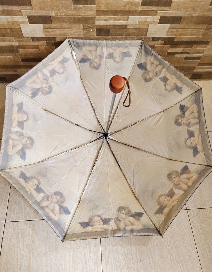 Raffaelo (Category: Umbrellas) located in Davao. Submitted by dvo_jpnstuff (Listing ID 1462059084, Image 3). Description: This is a compact Raffaello Cherubs folding umbrella featuring a classic Renaissance angel art print and a wooden-capped handle stored inside a clear plastic carrying case.