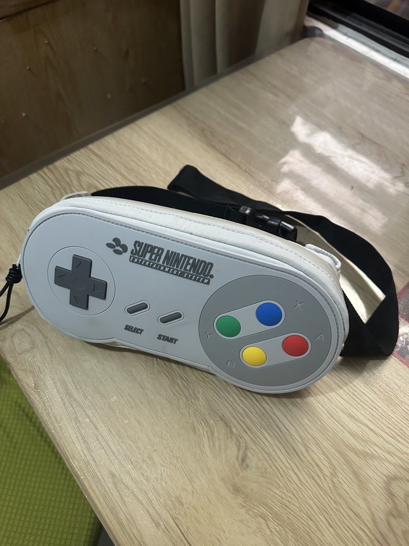 Super Nintendo Controller Pouch Bag (Category: Purses & Pouches) located in Manila. Submitted by naixor_thrift (Listing ID 1462092068, Image 1). Description: - Super Nintendo controller shaped pouch - Ideal for storing pens, makeup, or accessories - Features classic SNES button layout and logo - Made by Zara - Zipper closure with a strap - Fun retro gaming accessory.