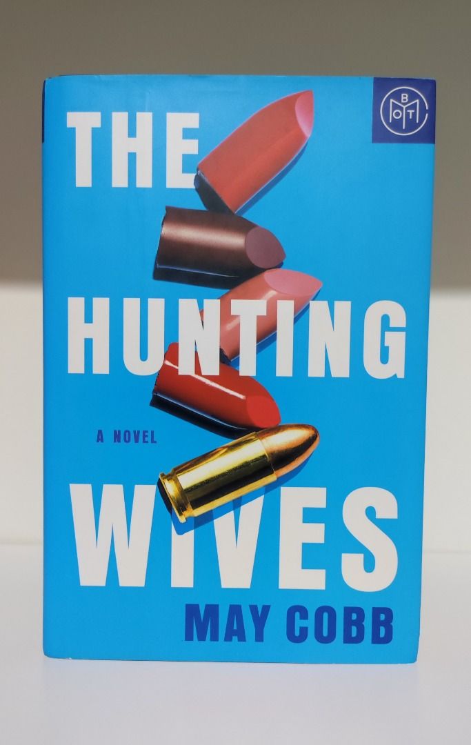 The Hunting Wives by May Cobb (BOTM) (Category: Storybooks) located in Agoo. Submitted by sweetluminescence (Listing ID 1462110691, Image 1). Description: 'The Hunting Wives' by May Cobb. It's a novel with a striking cover design featuring lipsticks and a bullet. Great for fans of thrillers or suspense..