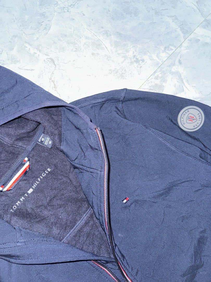 Tommy Hilfiger Navy Blue Hooded Jacket Size M (Category: Coats, Jackets and Outerwear) located in Manila. Submitted by tanlaxfinds (Listing ID 1462047049, Image 2). Description: - Navy blue Tommy Hilfiger hooded jacket - Made of 100% polyester - Fleece-lined interior for warmth - Full zip front closure - Two zippered pockets - Small Tommy Hilfiger logo on chest - Tommy Hilfiger patch on sleeve - Ideal for cooler weather.