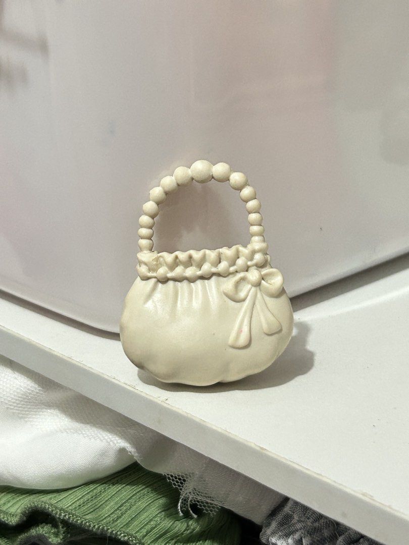 White Doll Handbag with Beaded Handle and Bow Detail (Category: Purses & Pouches) located in Batangas. Submitted by nommi26 (Listing ID 1462200577, Image 2). Description: - Adorable white handbag for dolls - Features a charming beaded handle - Decorated with a sweet bow on the front - Top edge has a delicate ruffled detail - Ideal accessory to complete any doll's outfit - Perfectly sized for small dolls needs cleaning.