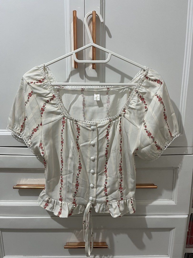 White Floral Puff Sleeve Square Neck Top (Category: Blouses) located in Pili. Submitted by jhamimin22 (Listing ID 1462149362, Image 1). Description: - Adorable white top with a charming floral print and subtle vertical stripes. - Features a flattering square neckline adorned with delicate lace trim. - Feminine puff sleeves add a touch of sweetness. - Functional buttons down the front for easy wear. - Adjustable tie at the hem for a customized fit