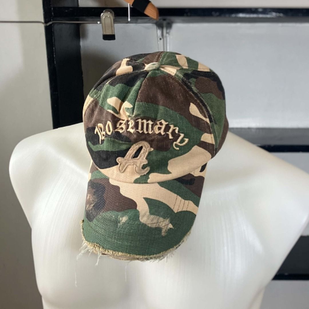 Y2K Grunge Roseman Distressed Camo Baseball Cap (Category: Hats & Beanies) located in Manila. Submitted by nellyfrustrado (Listing ID 1462174675, Image 1). Description: * Brand: Roseman * Style: 6-Panel Distressed Camouflage Baseball Cap. Features raised gothic script "Roseman" embroidery on the crown and a heavily frayed, raw-edge brim. * Material: Heavyweight cotton canvas in a classic woodland camo print, finished with a genuine leather adjust