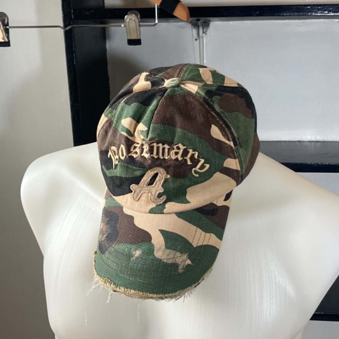 Y2K Grunge Roseman Distressed Camo Baseball Cap (Category: Hats & Beanies) located in Manila. Submitted by nellyfrustrado (Listing ID 1462174675, Image 2). Description: * Brand: Roseman * Style: 6-Panel Distressed Camouflage Baseball Cap. Features raised gothic script "Roseman" embroidery on the crown and a heavily frayed, raw-edge brim. * Material: Heavyweight cotton canvas in a classic woodland camo print, finished with a genuine leather adjust