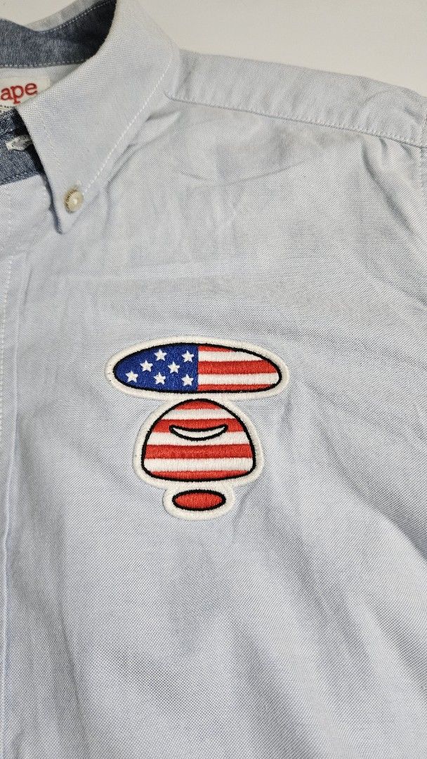 Aape by A Bathing Ape Blue Button Down Shirt (Category: Tshirts & Polo Shirts ) located in Alfonso. Submitted by jbcamet (Listing ID 1462415519, Image 3). Description: - Brand: Aape by A Bathing Ape - Color: Light Blue - Material: 100% Cotton - Design: Button-down shirt - Features: Embroidered American flag patch on chest, Aape logo print on hem - Collar: Classic button-down - Cuffs: Button cuffs.