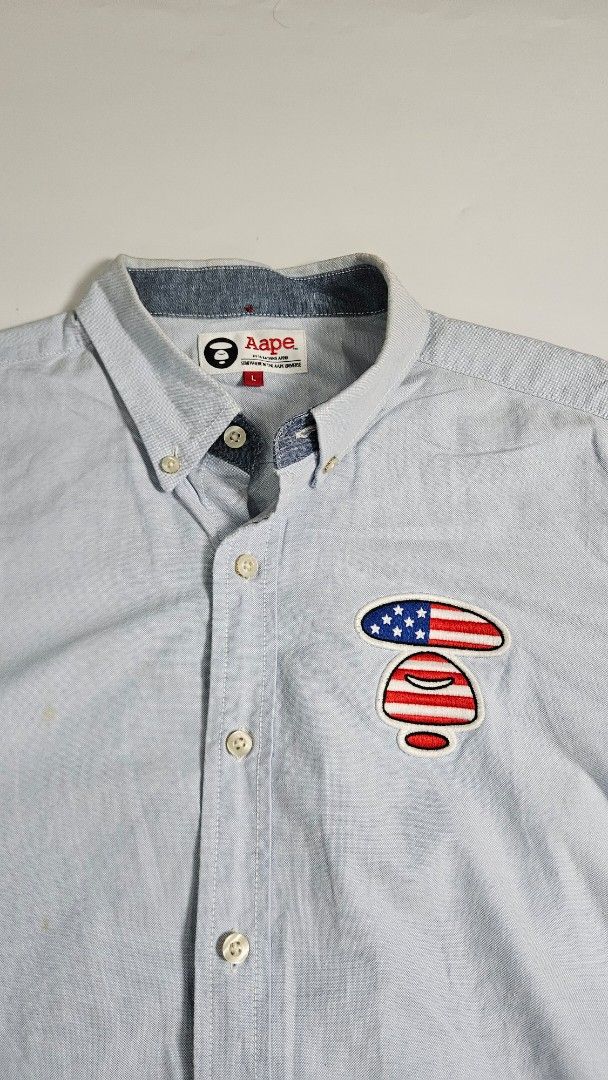Aape by A Bathing Ape Blue Button Down Shirt (Category: Tshirts & Polo Shirts ) located in Alfonso. Submitted by jbcamet (Listing ID 1462415519, Image 2). Description: - Brand: Aape by A Bathing Ape - Color: Light Blue - Material: 100% Cotton - Design: Button-down shirt - Features: Embroidered American flag patch on chest, Aape logo print on hem - Collar: Classic button-down - Cuffs: Button cuffs.