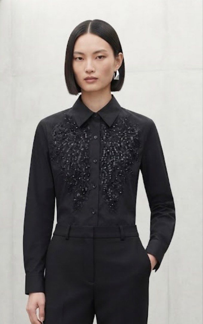 Black Sequined Wing Detail Button-Up Shirt (Category: Shirts) located in Donsol. Submitted by saksthriftavenuebyluckymaria8 (Listing ID 1462369156, Image 2). Description: - Black button-up shirt - Features sequined wing detail on the front - Long sleeves and collared - Perfect for dressing up or down - Looks great with trousers or a skirt - Ideal for evening wear or a statement office look Black long-sleeve button-up shirt featuring striking sequ