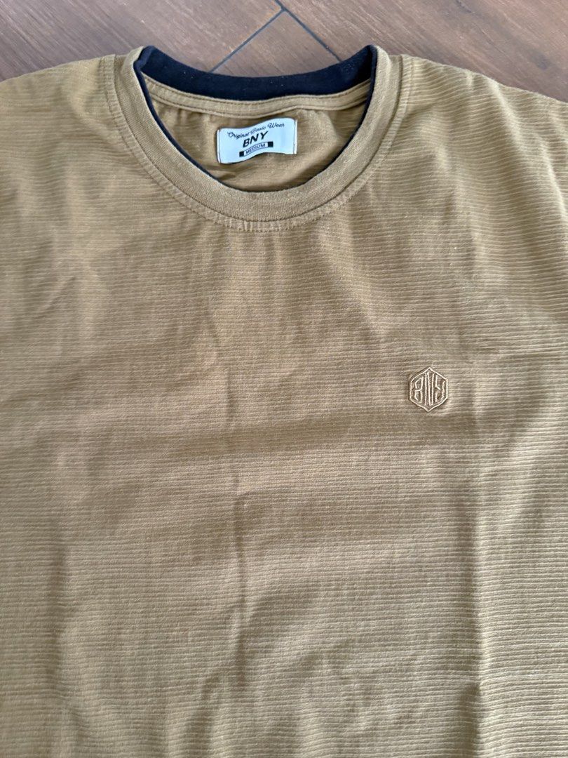 BNY Original Basic Wear T-shirt - Brown, Size Medium (Category: Babies & Kids Fashion) located in Bulacan. Submitted by emjay_17 (Listing ID 1462315536, Image 2). Description: - Brand: BNY Original Basic Wear - Color: Chocolate Brown - Fabric: Textured with subtle vertical stripes - Design: Small embroidered logo on chest - Neckline: Crew neck with dark trim - Sleeves: Short sleeves with dark trim - Occasion: Ideal for casual wear.