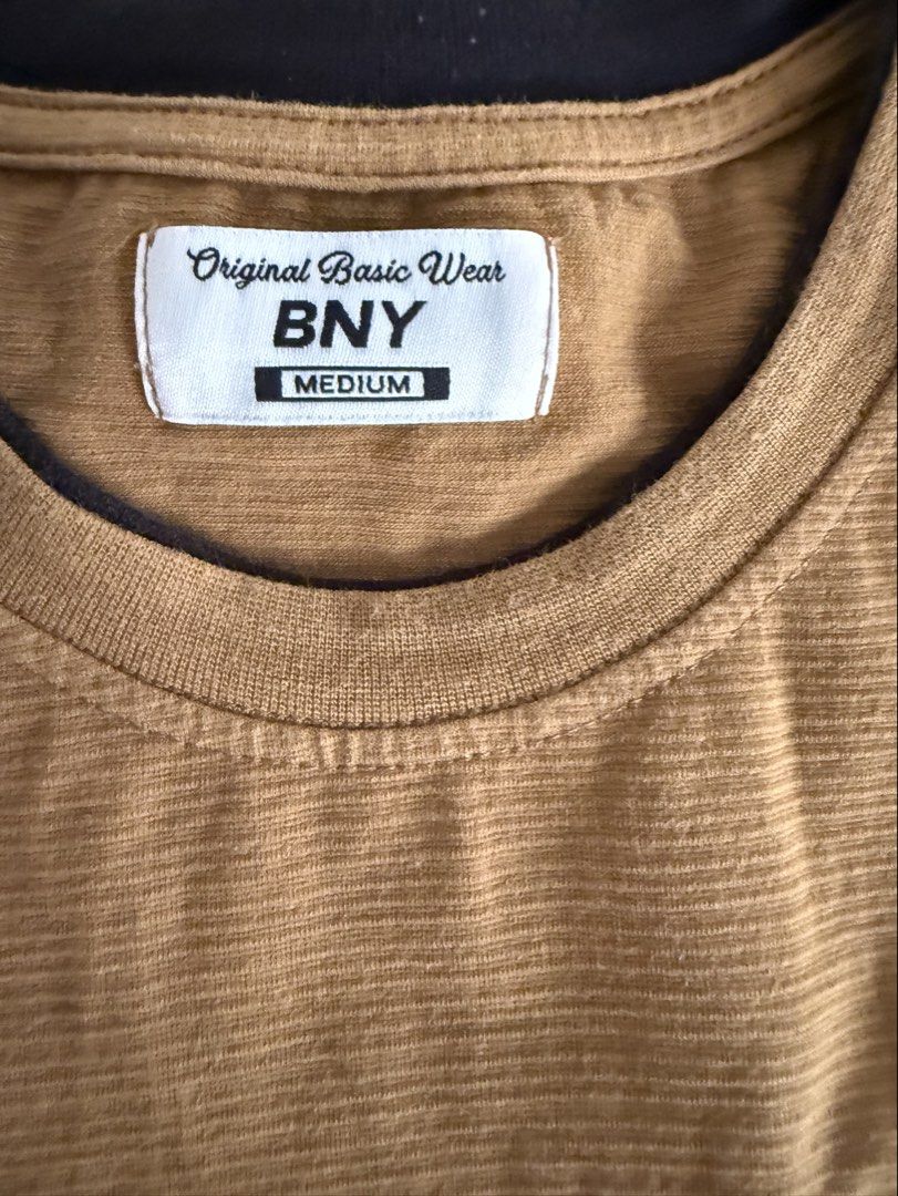BNY Original Basic Wear T-shirt - Brown, Size Medium (Category: Babies & Kids Fashion) located in Bulacan. Submitted by emjay_17 (Listing ID 1462315536, Image 1). Description: - Brand: BNY Original Basic Wear - Color: Chocolate Brown - Fabric: Textured with subtle vertical stripes - Design: Small embroidered logo on chest - Neckline: Crew neck with dark trim - Sleeves: Short sleeves with dark trim - Occasion: Ideal for casual wear.