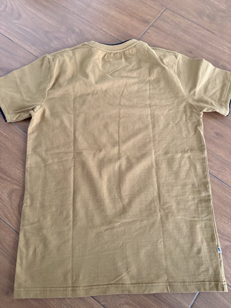 BNY Original Basic Wear T-shirt - Brown, Size Medium (Category: Babies & Kids Fashion) located in Bulacan. Submitted by emjay_17 (Listing ID 1462315536, Image 3). Description: - Brand: BNY Original Basic Wear - Color: Chocolate Brown - Fabric: Textured with subtle vertical stripes - Design: Small embroidered logo on chest - Neckline: Crew neck with dark trim - Sleeves: Short sleeves with dark trim - Occasion: Ideal for casual wear.