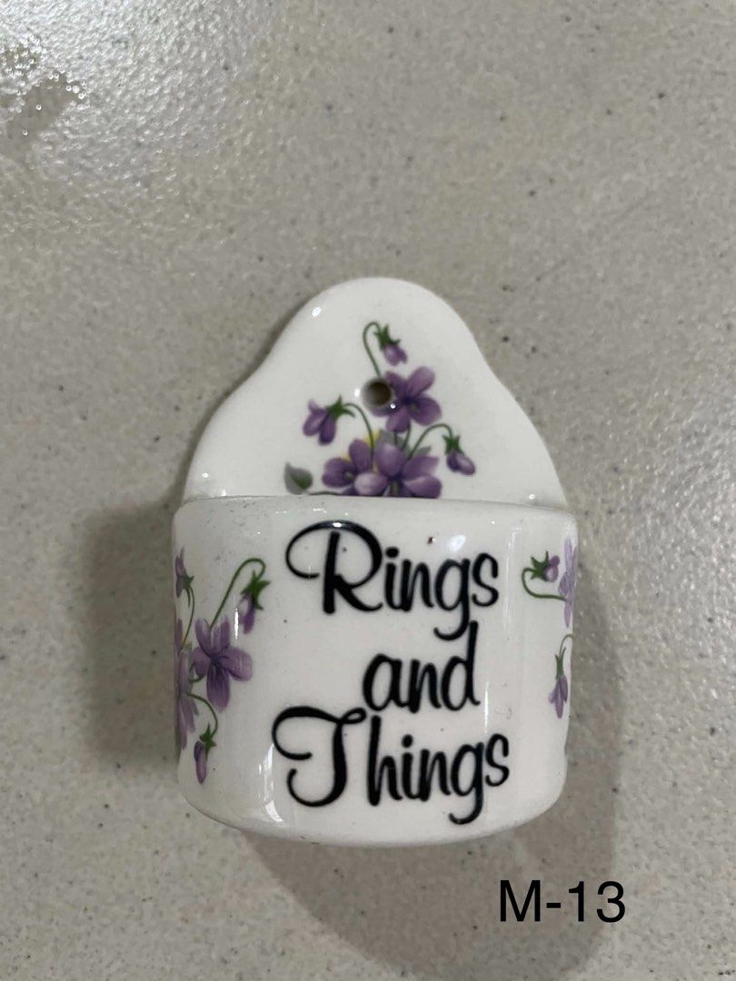 Ceramic Wall Pocket "Rings and Things" with Floral Design (Category: Wall Decor) located in Quezon City. Submitted by meggoquingco (Listing ID 1462340635, Image 1). Description: - Cute ceramic wall pocket - "Rings and Things" inscription - Decorated with pretty purple flowers - Ideal for holding small items (jewelry, keys, etc.) - Can be hung on a wall - Dimensions: Approx. 2.5 inches tall, 2 inches wide at opening - Perfect for bedroom or entryw