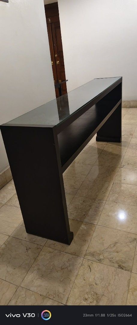 Dark Wood Console Table with Glass Top (Category: Tables & Sets) located in Taguig. Submitted by thrifthub.ph (Listing ID 1462291176, Image 2). Description: CONDO PULL-OUT!! NEED TO DISPOSED ASAP!! Elegant dark wood console table with clear glass top and open shelf. Perfect for entryways or behind sofas. 1.5m long. Selling due to redecoration..