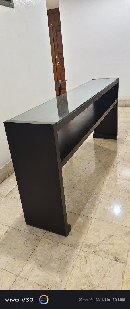 Dark Wood Console Table with Glass Top (Category: Tables & Sets) located in Taguig. Submitted by thrifthub.ph (Listing ID 1462291176, Image 1). Description: CONDO PULL-OUT!! NEED TO DISPOSED ASAP!! Elegant dark wood console table with clear glass top and open shelf. Perfect for entryways or behind sofas. 1.5m long. Selling due to redecoration..