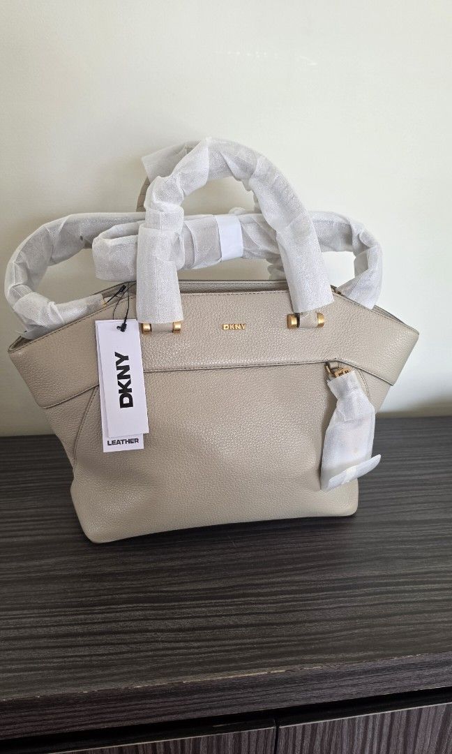 DKNY RAEGAN SATCHEL (Category: Luxury Bags & Wallets) located in Makati City. Submitted by dollymeng (Listing ID 1462308878, Image 1). Description: Elevate your everyday style with the DKNY RAEGAN Medium Satchel in timeless beige. Crafted from luxurious 100% cow leather, this sophisticated top handle bag offers spacious compartments and elegant gold-tone accents, making it the perfect accessory for polished, effortless chic..