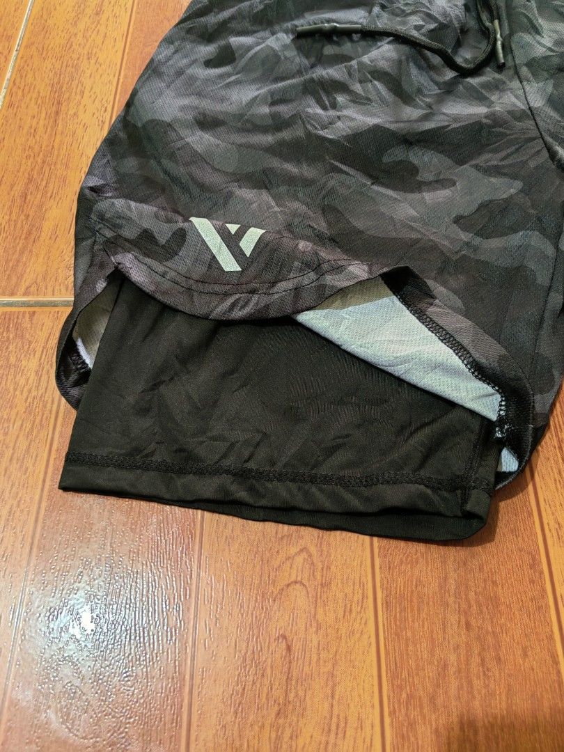 Men's Camo Athletic Shorts with Inner Liner (Category: Shorts) located in Matnog. Submitted by erasmoarnold.b9c007 (Listing ID 1462308553, Image 3). Description: - Dark grey camouflage shorts - Built-in black liner for support - Elastic waistband with adjustable drawstring - Versatile for workouts or casual wear - Features a logo on the left leg.