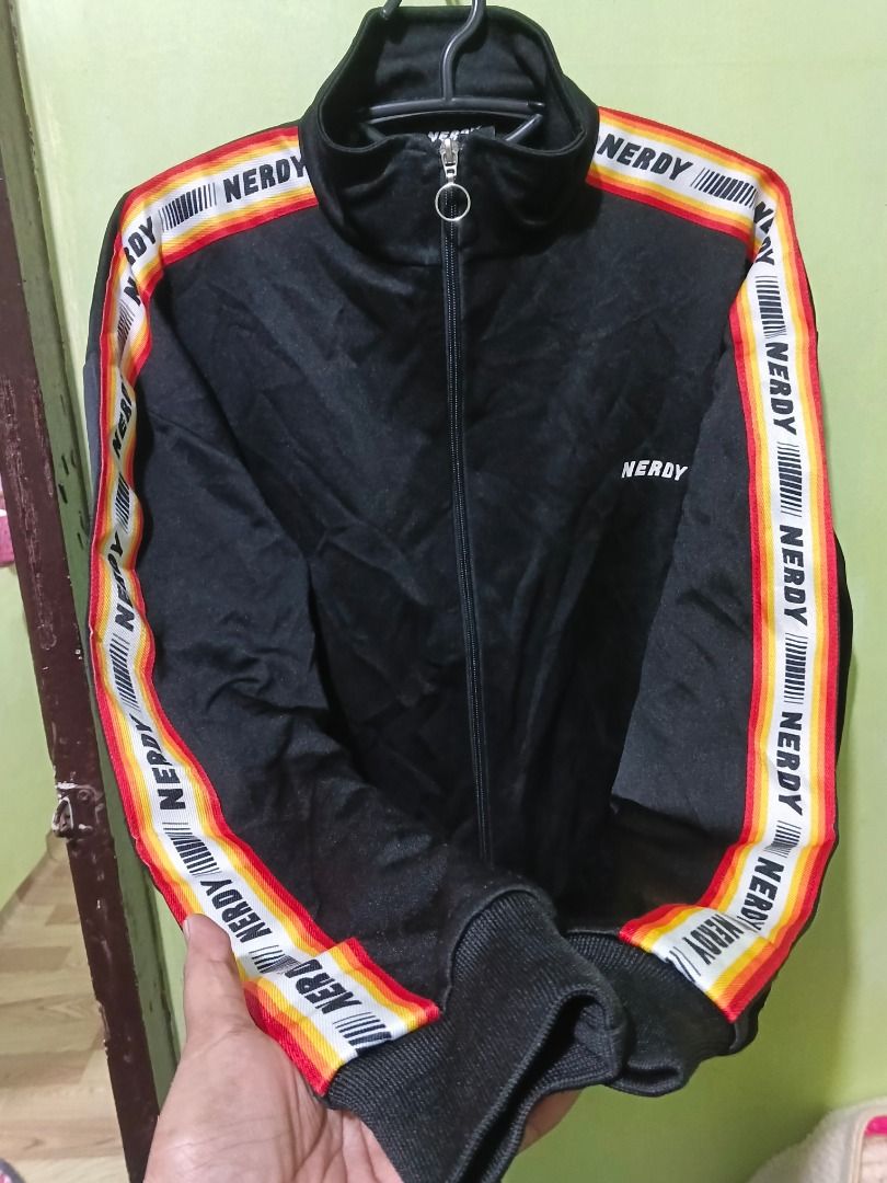 NERDY Black Track Jacket with Striped Sleeves (Category: Coats, Jackets and Outerwear) located in Urdaneta. Submitted by fastbird.12354e (Listing ID 1462327290, Image 2). Description: - Dimension: 22 x 26 - Brand: NERDY - Color: Black - Design: Brand name on chest and sleeves, colorful stripe detail - Features: Full zip front, stand-up collar, ribbed cuffs and hem - Style: Ideal for casual wear or sports.