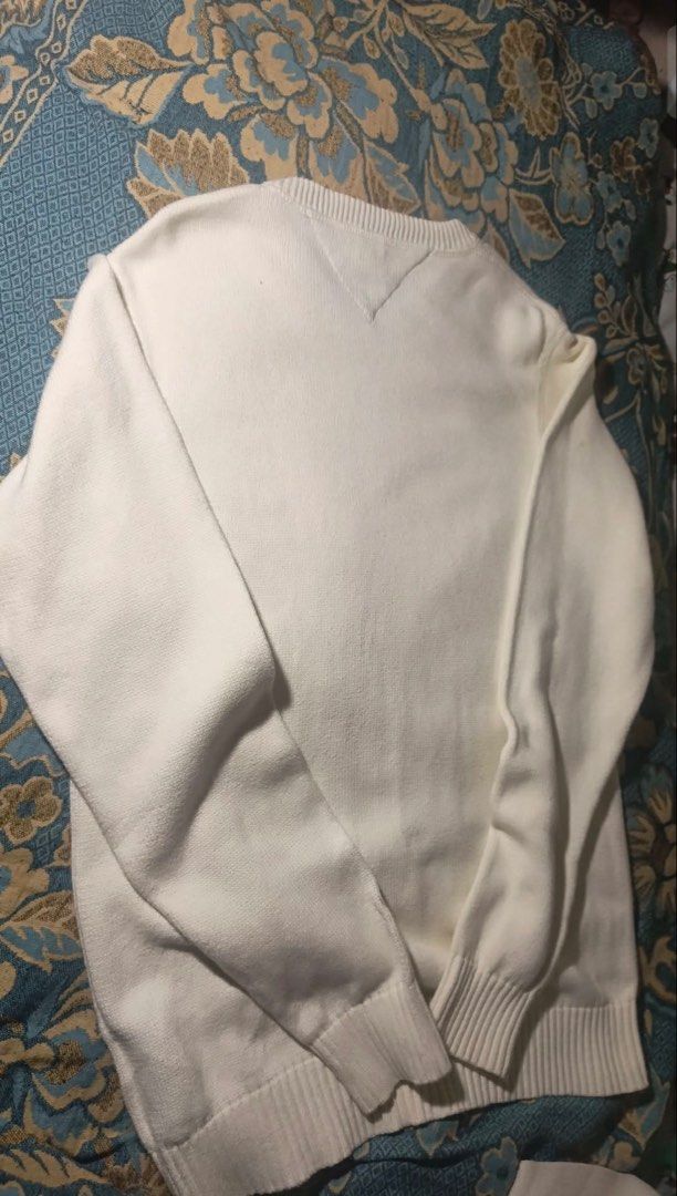 Tommy Hilfiger Sweater (Category: Coats, Jackets and Outerwear) located in Manila. Submitted by jenii_collective (Listing ID 1462406374, Image 2). Description: - Classic white V-neck sweater - Brand: Tommy Hilfiger - Material: Knitted - Features: Ribbed cuffs and hem, small embroidered logo on chest - Style: Versatile, great for layering or wearing alone.