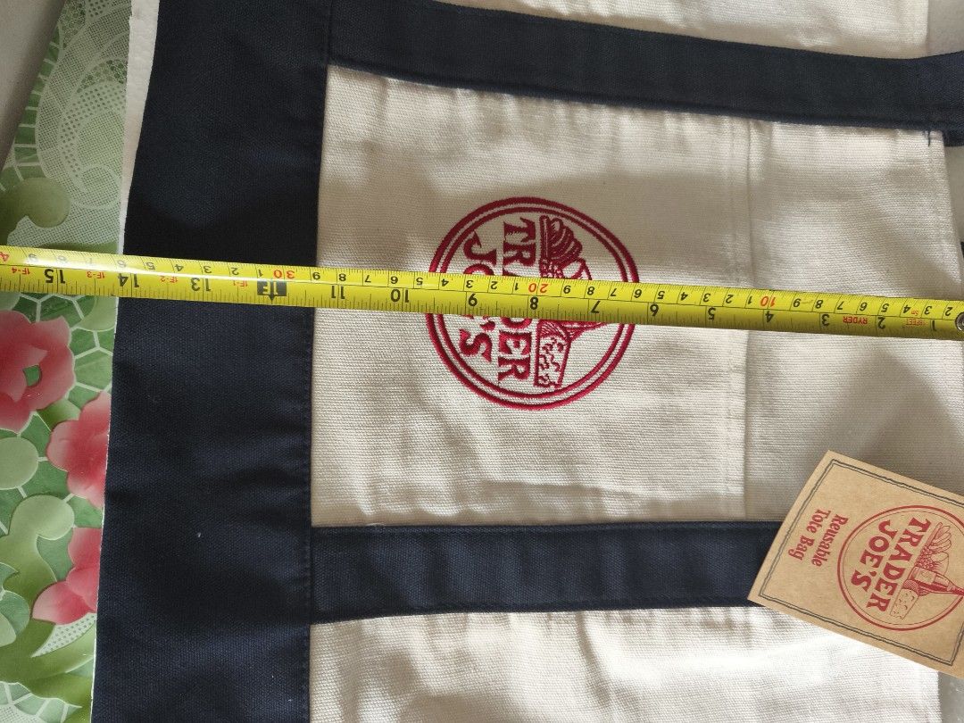 Trader Joe's Reusable Canvas Tote Bag (Category: Tote Bags) located in San Juan City. Submitted by vingabby (Listing ID 1462292658, Image 2). Description: - Classic Trader Joe's reusable tote bag - Cream canvas with navy blue trim and handles - Iconic Trader Joe's logo embroidered on front - Features a handy front pocket - Great for groceries or everyday use - Measures approximately 19 inches wide.
