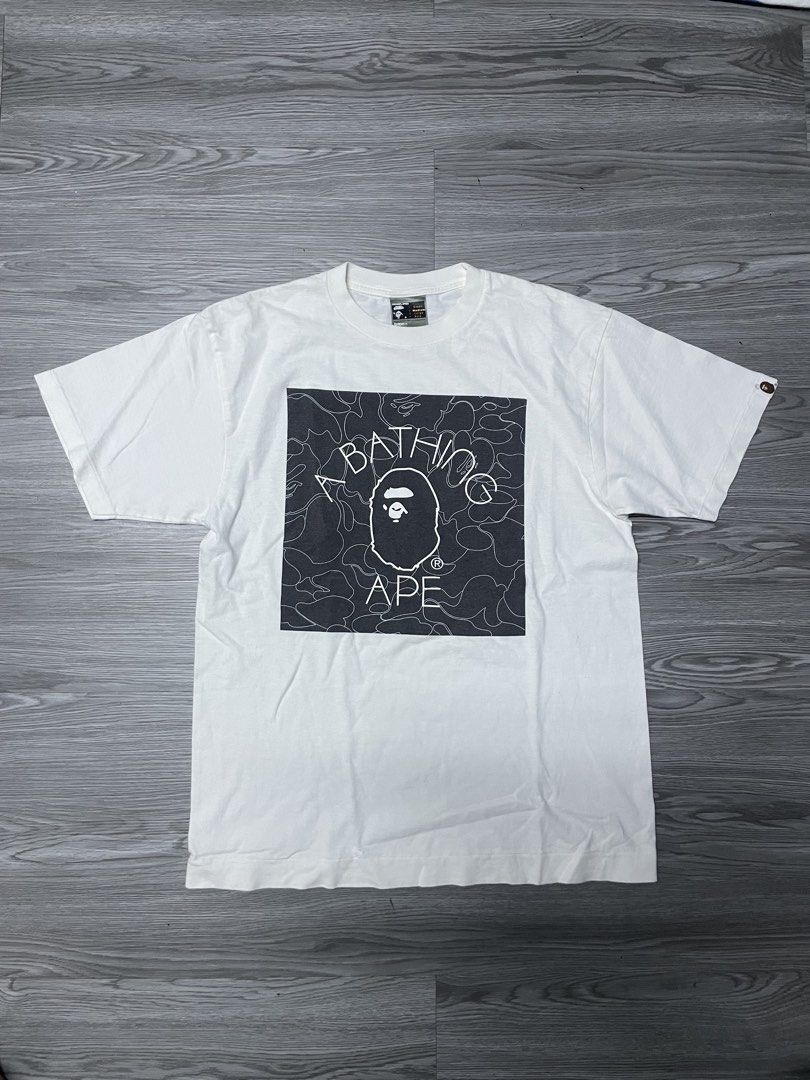 A Bathing Ape BAPE Tee White (Category: Tshirts & Polo Shirts ) located in Manila. Submitted by yourfavoriteplug (Listing ID 1462508440, Image 1). Description: - White BAPE T-shirt - Classic ape head logo graphic - Signature camo pattern in background - Tagged size Medium - Essential for any streetwear collection.