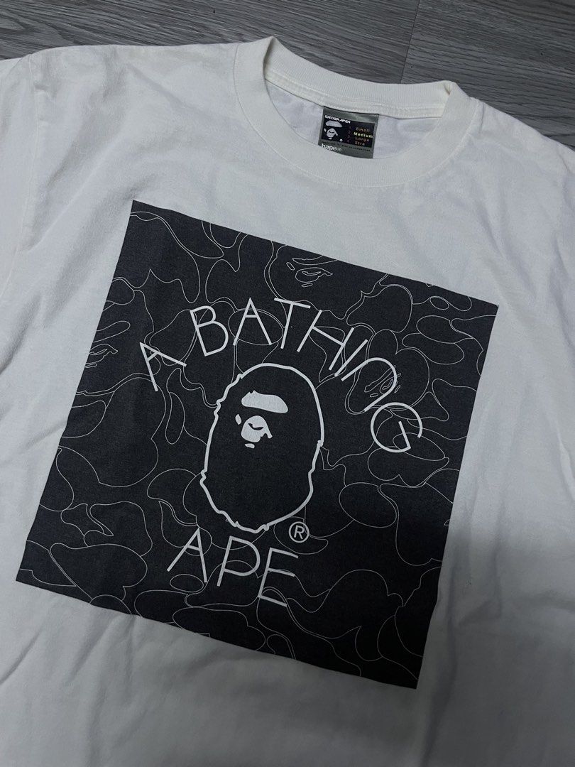 A Bathing Ape BAPE Tee White (Category: Tshirts & Polo Shirts ) located in Manila. Submitted by yourfavoriteplug (Listing ID 1462508440, Image 2). Description: - White BAPE T-shirt - Classic ape head logo graphic - Signature camo pattern in background - Tagged size Medium - Essential for any streetwear collection.