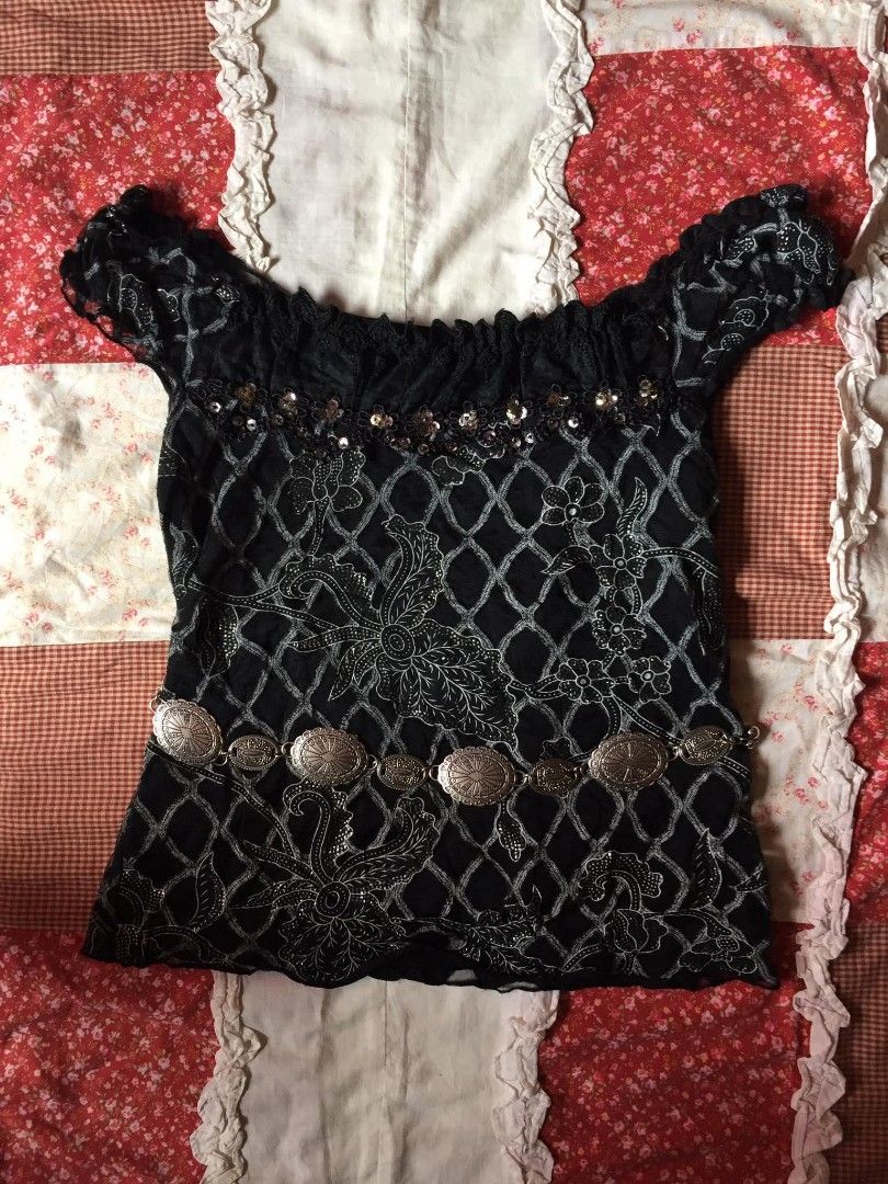 Black Off-Shoulder Top with Sequins and Embellishments (Category: Blouses) located in Aloran. Submitted by thriftfinds.co (Listing ID 1462533400, Image 1). Description: - Black off-shoulder top - Short sleeves with ruffled edges - Neckline adorned with lace trim and sequins - Unique patterned fabric with diamond net overlay - Comes with a silver-tone decorative belt - Fun and eye-catching piece.
