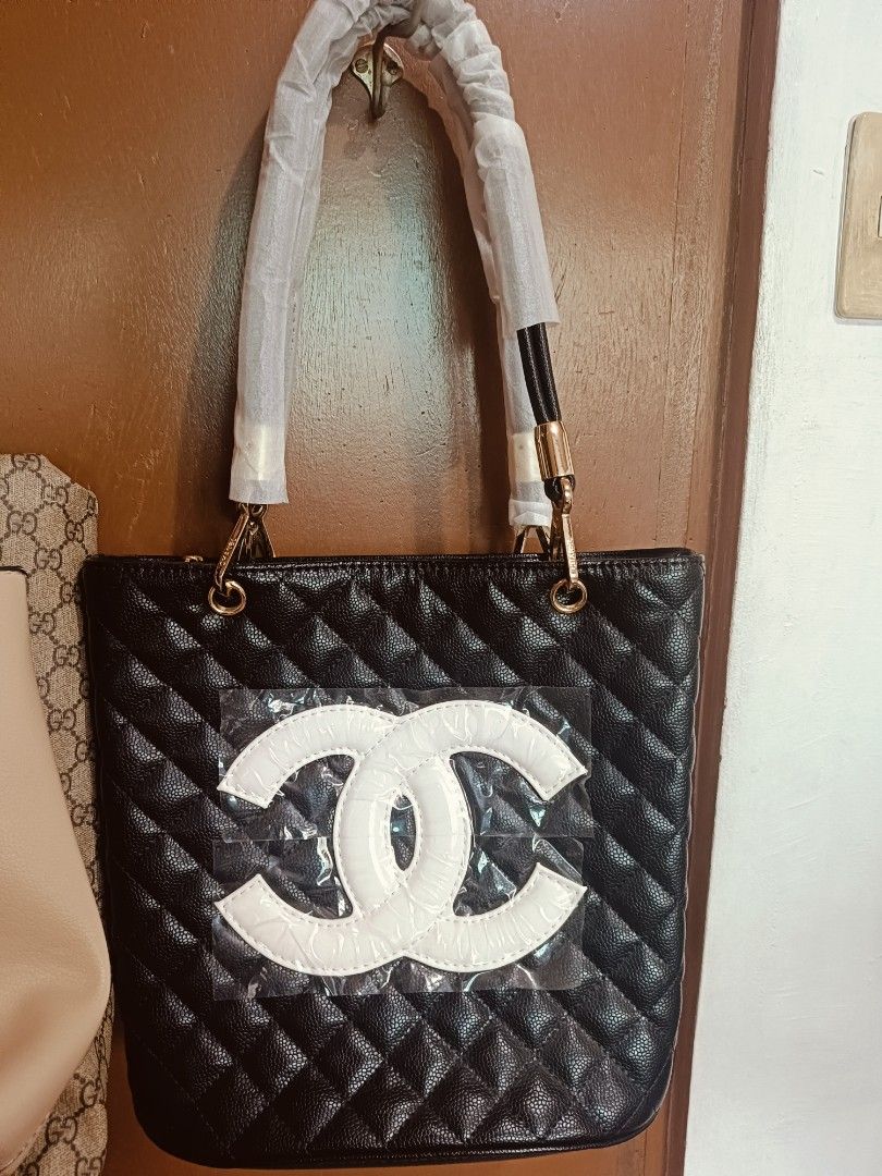 Black Quilted Tote Bag with White CC Logo (Category: Tote Bags) located in Quezon City. Submitted by chowpow (Listing ID 1462450348, Image 1). Description: - Classic black quilted tote bag - Features a large white CC logo on the front - Gold hardware details - Handles are wrapped in protective plastic - Versatile for everyday or special occasions.