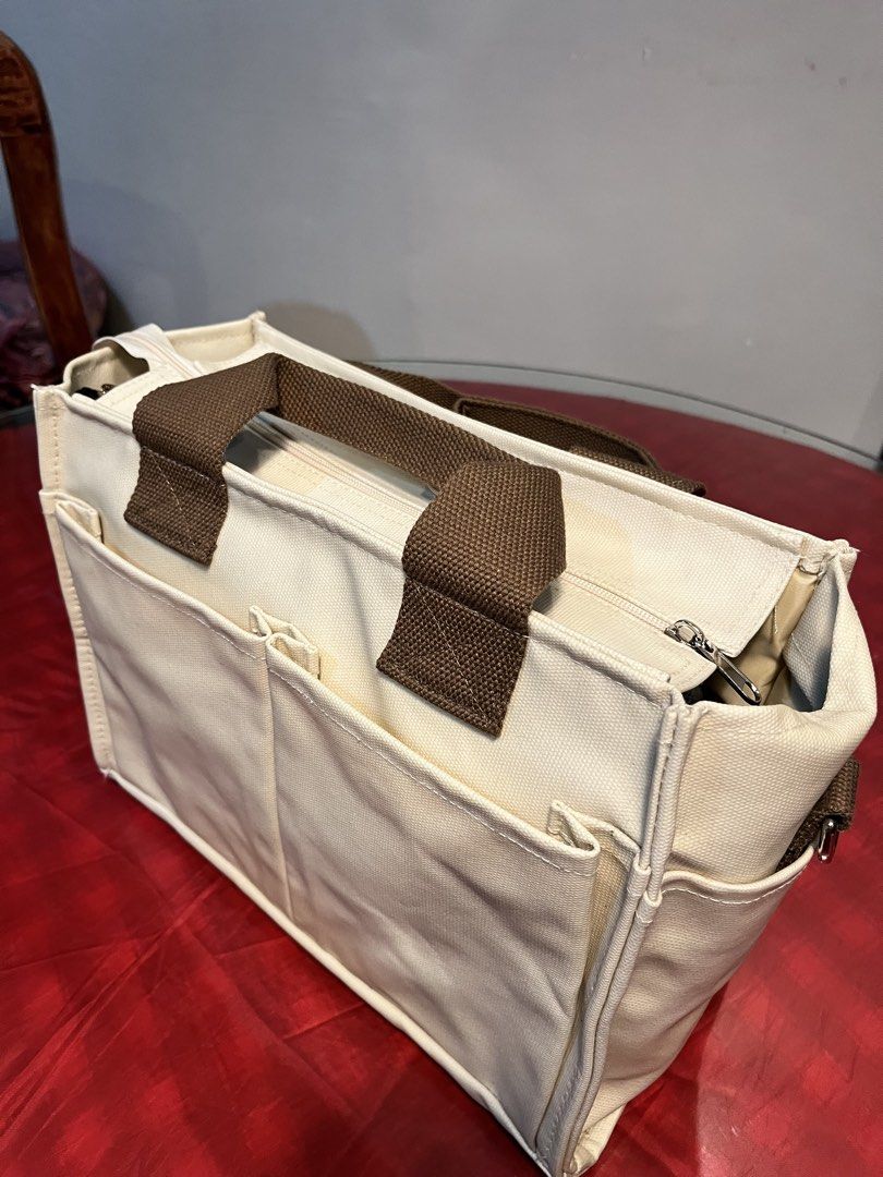 Canvas Tote Bag with Multiple Pockets (Category: Tote Bags) located in Manila. Submitted by harpymonetttt (Listing ID 1462650785, Image 2). Description: - Cream colored canvas tote bag - Brown canvas handles and strap - Multiple exterior pockets (front and sides) - Interior features: zippered pocket and main compartment - Secure top zipper closure - Ideal for everyday use or travel.