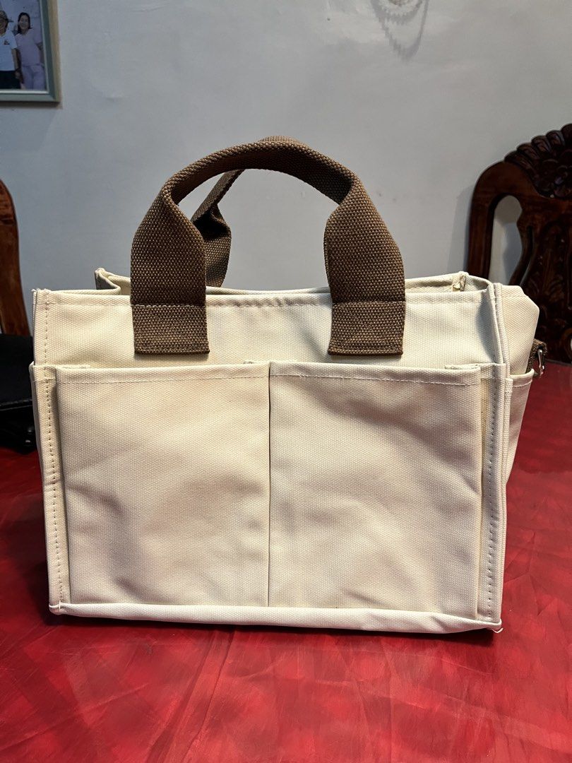 Canvas Tote Bag with Multiple Pockets (Category: Tote Bags) located in Manila. Submitted by harpymonetttt (Listing ID 1462650785, Image 1). Description: - Cream colored canvas tote bag - Brown canvas handles and strap - Multiple exterior pockets (front and sides) - Interior features: zippered pocket and main compartment - Secure top zipper closure - Ideal for everyday use or travel.