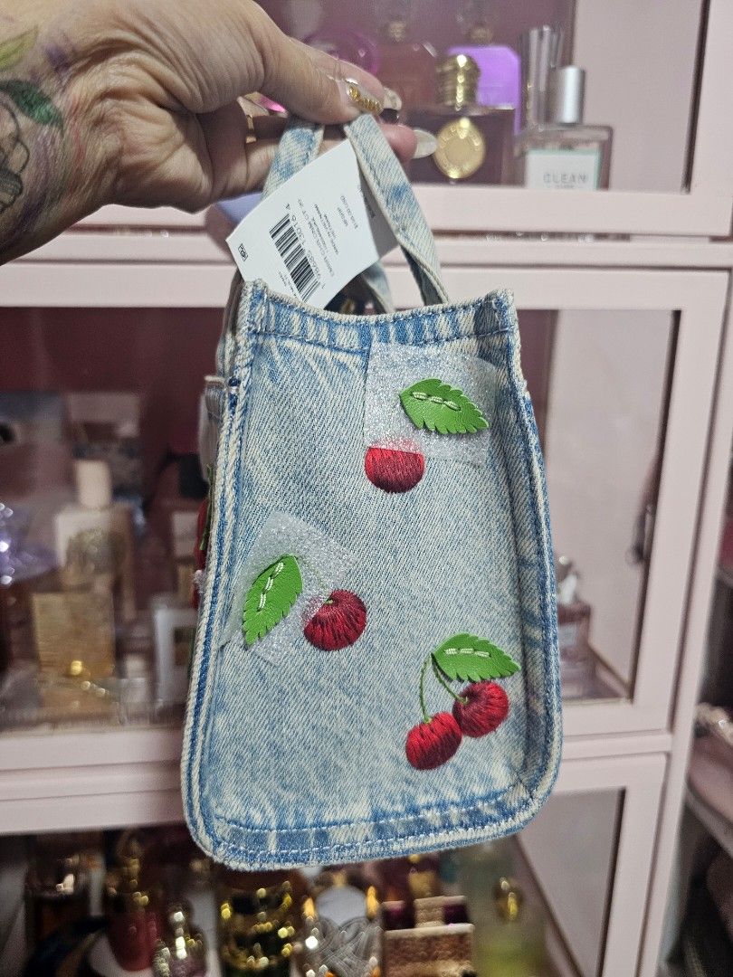 Coach New York Denim Cherry Mini Tote Bag (Category: Luxury Bags & Wallets) located in Angeles City. Submitted by kodachi10 (Listing ID 1440151713, Image 3). Description: - Authentic Coach New York mini tote bag - Light wash denim material - Charming all-over embroidered cherry motif - Secure turn-lock closure - Detachable leather hangtag - Perfect for adding a fun pop to your outfit - Bought in the US at retail price - Comes with sling.