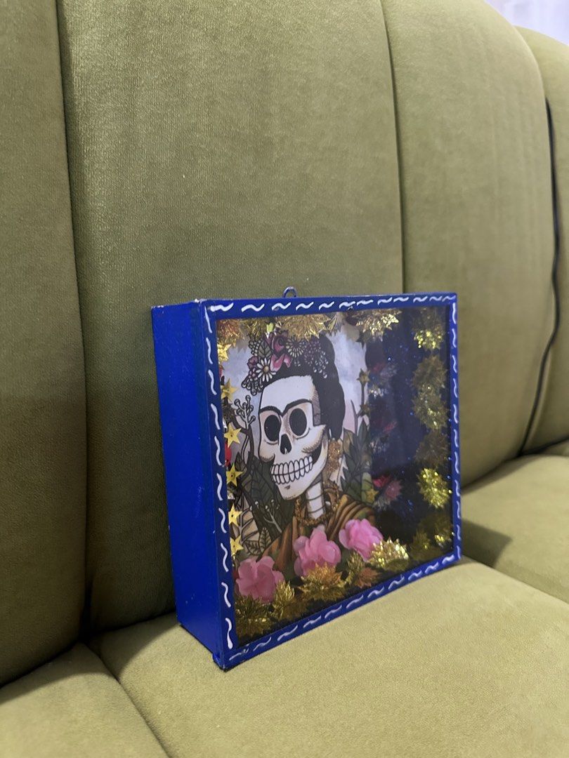 Frida Kahlo Shadow Box Art FROM MEXICO (Category: Art & Prints) located in Las Pinas. Submitted by petiteclothes_2000 (Listing ID 1462549577, Image 3). Description: - Handmade shadow box with a Frida Kahlo-inspired skeleton portrait. - Adorned with beautiful flowers, stars, and glittery accents. - Encased in a vibrant blue frame. - Ideal for unique home decor or as a thoughtful gift..