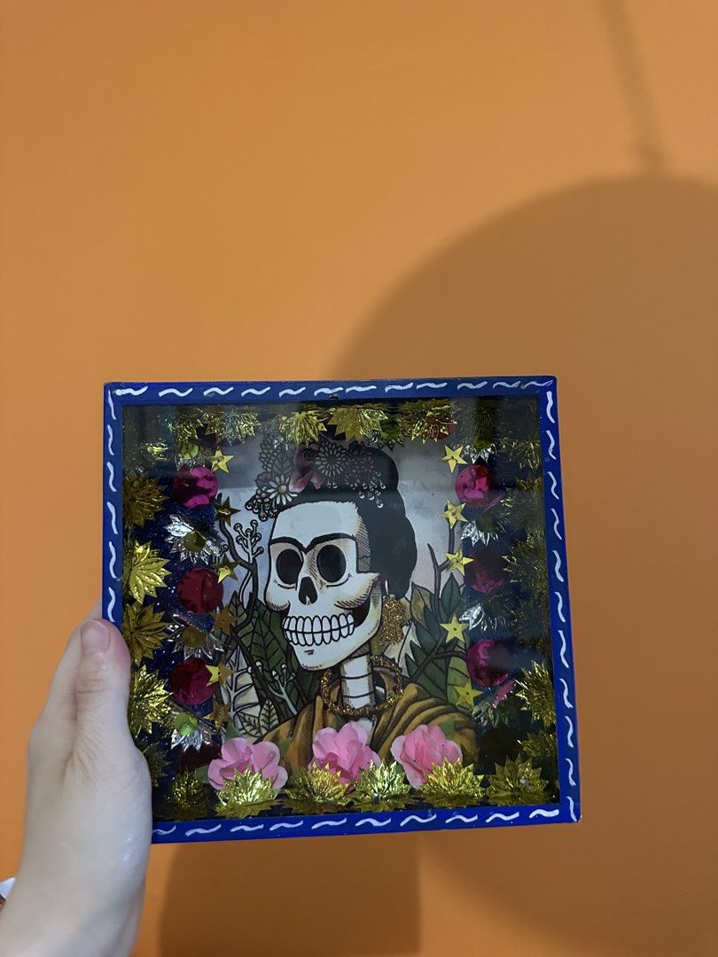 Frida Kahlo Shadow Box Art FROM MEXICO (Category: Art & Prints) located in Las Pinas. Submitted by petiteclothes_2000 (Listing ID 1462549577, Image 1). Description: - Handmade shadow box with a Frida Kahlo-inspired skeleton portrait. - Adorned with beautiful flowers, stars, and glittery accents. - Encased in a vibrant blue frame. - Ideal for unique home decor or as a thoughtful gift..