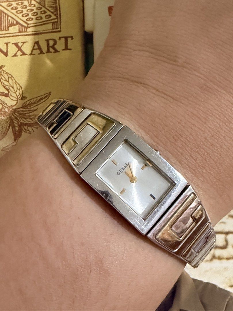 Guess women’s rectangular two-tone quartz watch. (Category: Women's Watches) located in Pasig City. Submitted by smartshopping.ph (Listing ID 1462455618, Image 1). Description: Guess women’s rectangular two-tone quartz watch. A sleek, rectangular stainless steel case framing a minimalist silver/white sunburst dial. It features simple gold-tone hour markers at the 12, 3, 6, and 9 o’clock positions with gold-tone hands. An integrated solid-link cuf