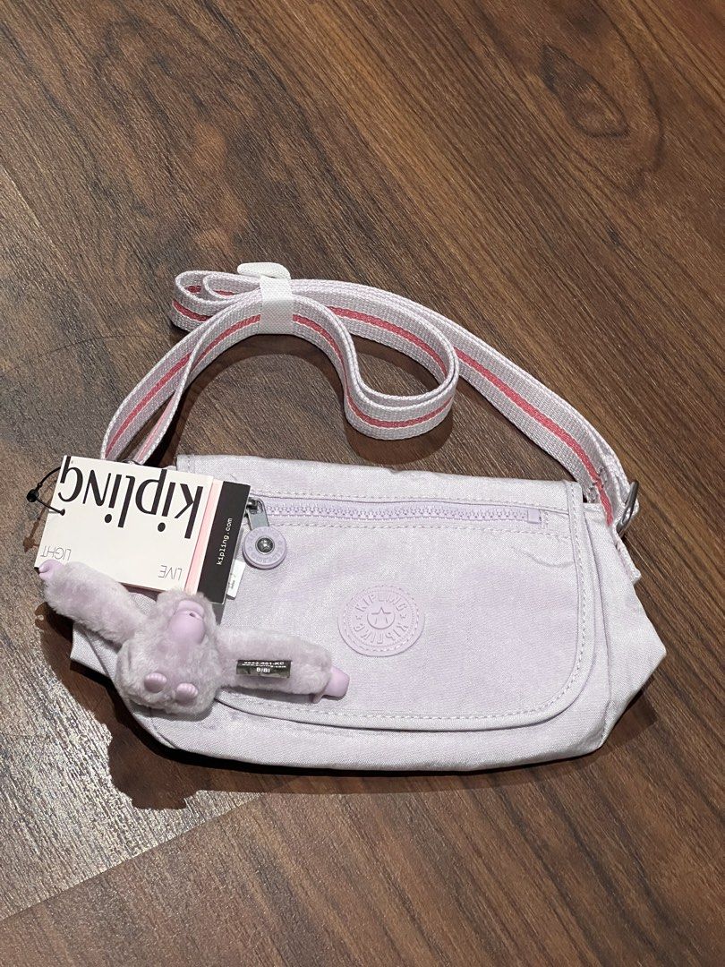 Kipling Abanu Crossbody Bag with Monkey Charm (Category: Cross-body Bags) located in Quezon City. Submitted by cmrls (Listing ID 1462628023, Image 2). Description: - Light purple original Kipling crossbody bag - Brand new with tag still attached - Adjustable strap with pink and white stripes - Secure zipper closure on top - Convenient front flap pocket - Iconic Kipling monkey charm included - Kipling logo prominently displayed on the front.