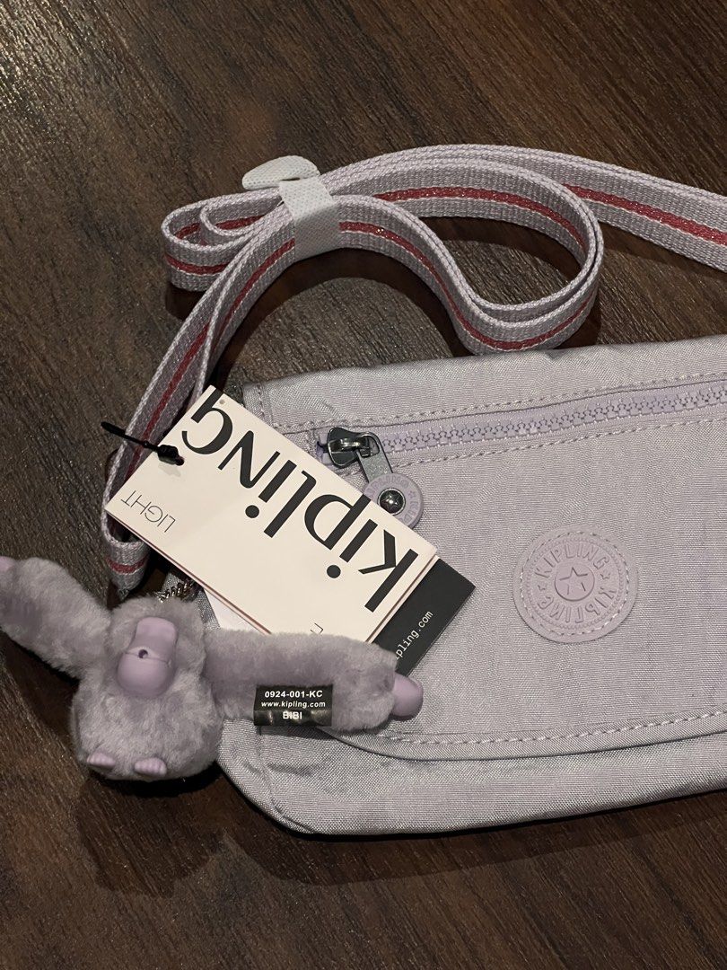 Kipling Abanu Crossbody Bag with Monkey Charm (Category: Cross-body Bags) located in Quezon City. Submitted by cmrls (Listing ID 1462628023, Image 3). Description: - Light purple original Kipling crossbody bag - Brand new with tag still attached - Adjustable strap with pink and white stripes - Secure zipper closure on top - Convenient front flap pocket - Iconic Kipling monkey charm included - Kipling logo prominently displayed on the front.