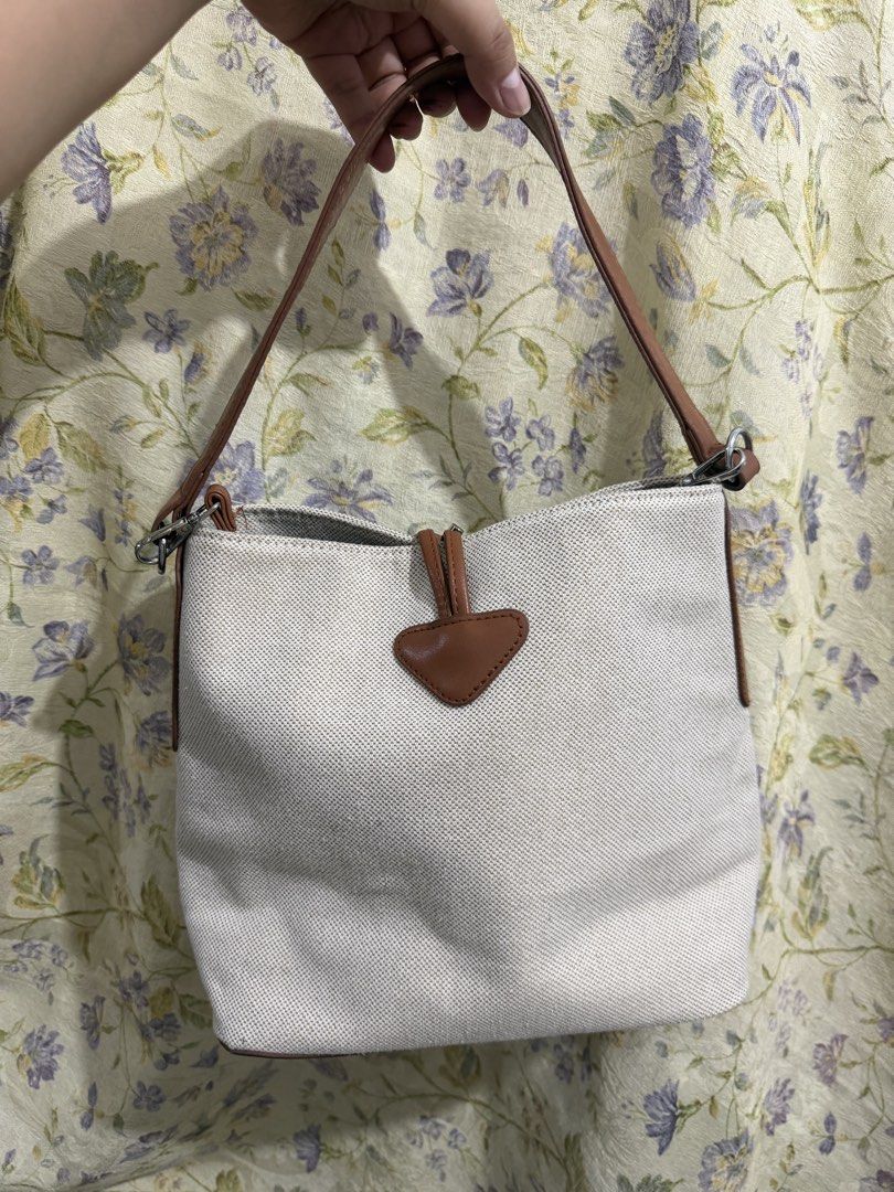 Longchamp Paris Canvas & Leather Bucket Bag (Category: Luxury Bags & Wallets) located in Binan City. Submitted by prelovedlagunaph (Listing ID 1462621114, Image 2). Description: - White canvas bucket bag - Brown leather accents and base - Longchamp Paris logo on front - Zipper closure with leather pull tab - Interior zippered and slip pockets - Adjustable shoulder strap.