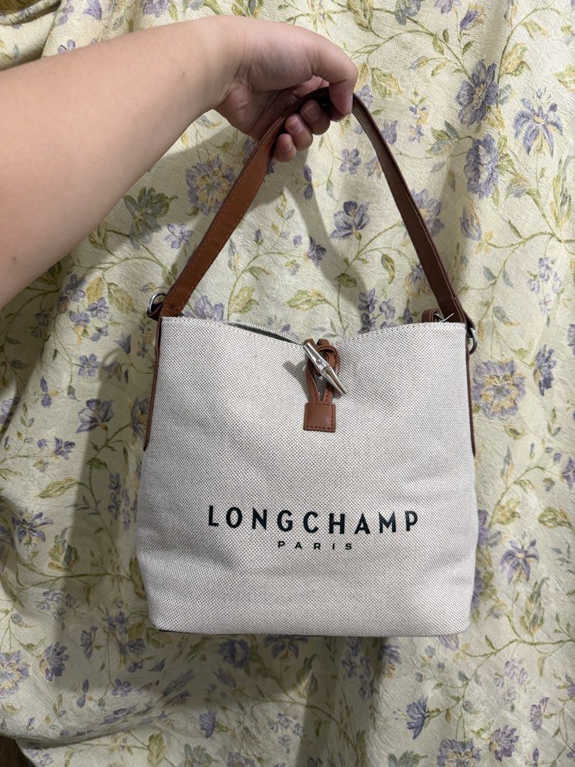 Longchamp Paris Canvas & Leather Bucket Bag (Category: Luxury Bags & Wallets) located in Binan City. Submitted by prelovedlagunaph (Listing ID 1462621114, Image 1). Description: - White canvas bucket bag - Brown leather accents and base - Longchamp Paris logo on front - Zipper closure with leather pull tab - Interior zippered and slip pockets - Adjustable shoulder strap.