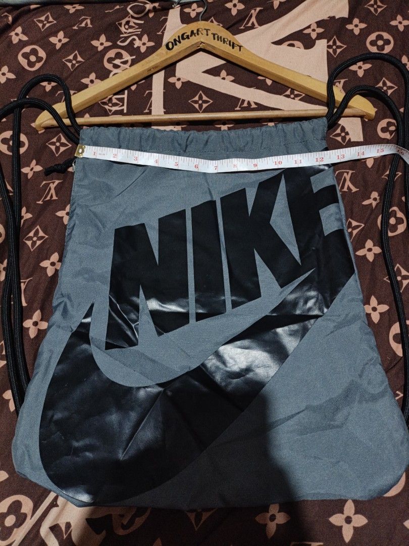 Nike Grey gym Drawstring Bag with Large Swoosh Logo (Category: Backpacks) located in Maasim. Submitted by ukayganda25 (Listing ID 1462631691, Image 3). Description: - Grey Nike drawstring bag - Large black Swoosh logo on front - Side zippered pocket for extra storage - Drawstring closure doubles as straps - Ideal for gym or everyday use - Approximate dimensions: 17" tall x 14" wide.