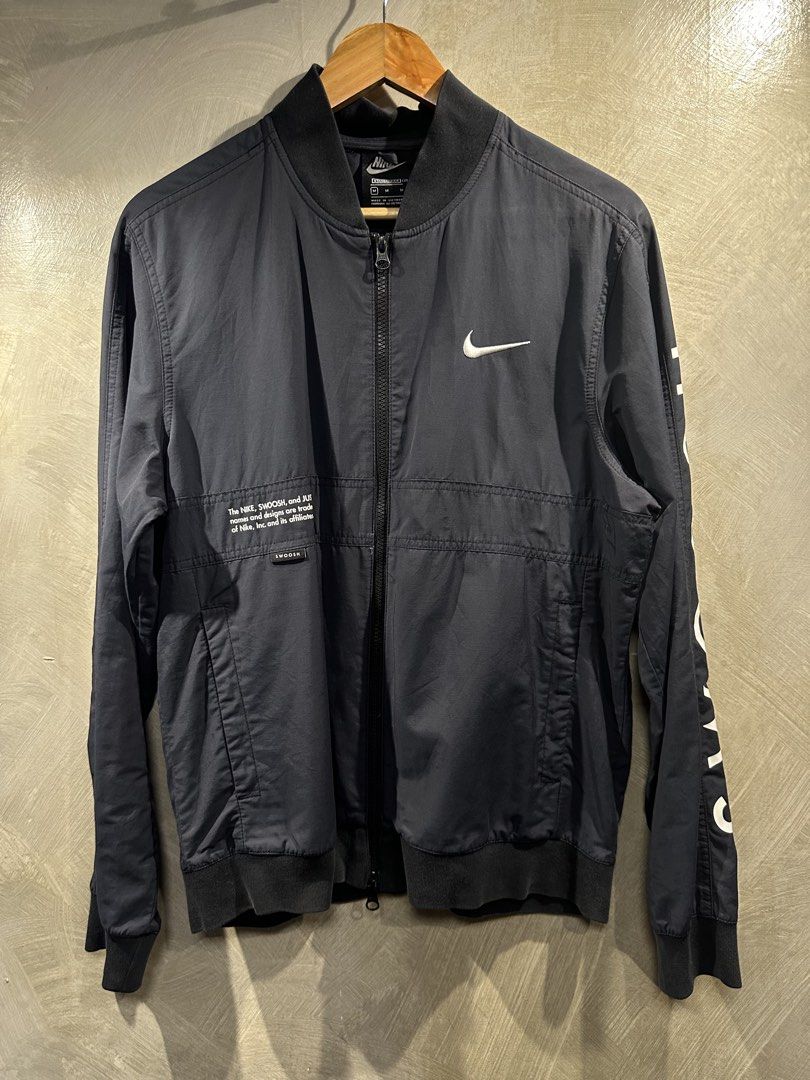 Nike Standard Fit Bomber Jacket (Category: Coats, Jackets and Outerwear) located in Manila. Submitted by gelo1999 (Listing ID 1462620868, Image 1). Description: - Navy blue Nike bomber jacket - Size: Medium (M) - Iconic Nike swoosh logo on the front - Large swoosh with text details on the back - Text graphics on the sleeve - Standard fit - Made in Vietnam - Note: Small mark on the front, as shown in the last photo..