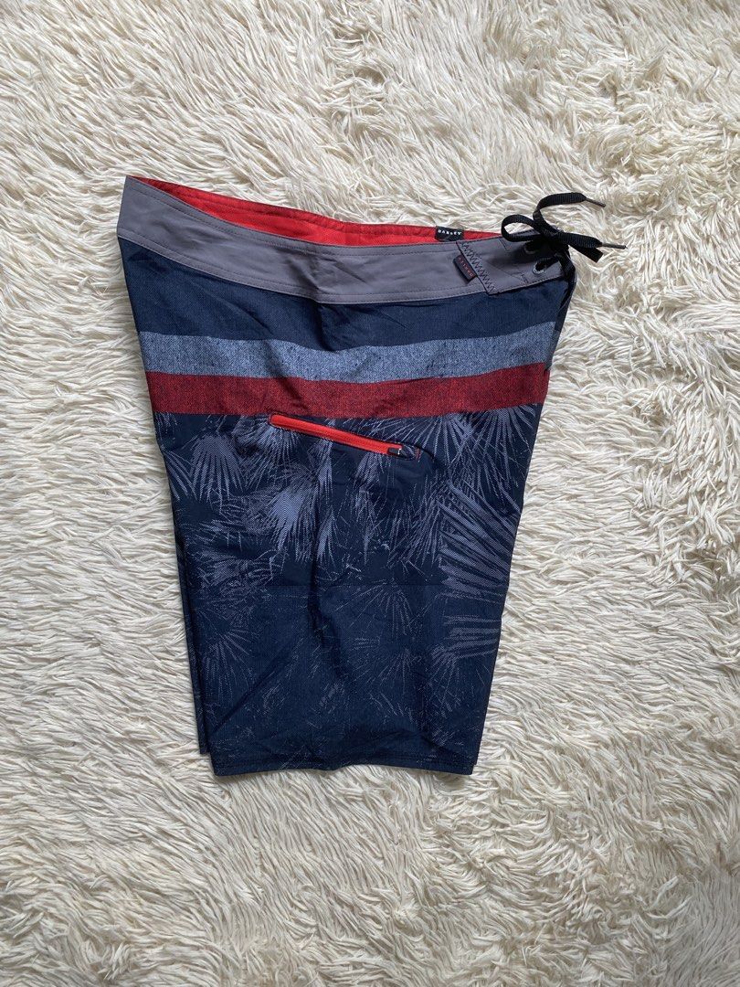 Oakley Board Shorts Size 32 (Category: Swim Trunks & Board Shorts) located in Antipolo. Submitted by switchneighborhood (Listing ID 1462470569, Image 3). Description: - Oakley board shorts - Size: 32 - Color: Dark blue with palm leaf print - Accents: Red and grey stripes - Features: Zippered pocket on left side, drawstring waist - Ideal for: Swimming, lounging, beach activities.
