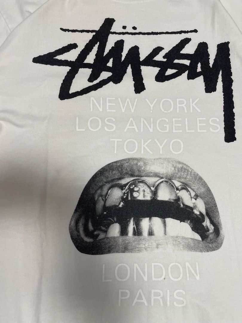 Stussy "World Tour" Graphic Tee (Category: Tshirts & Polo Shirts ) located in Manila. Submitted by cis_thrift143 (Listing ID 1462532599, Image 3). Description: - White Stussy graphic tee - Features the iconic 'World Tour' design with cities like New York, LA, Tokyo, London, and Paris - Unique graphic of lips with grills - Rick Owens logo on the back - Size: Medium (M) - Made in Mexico.