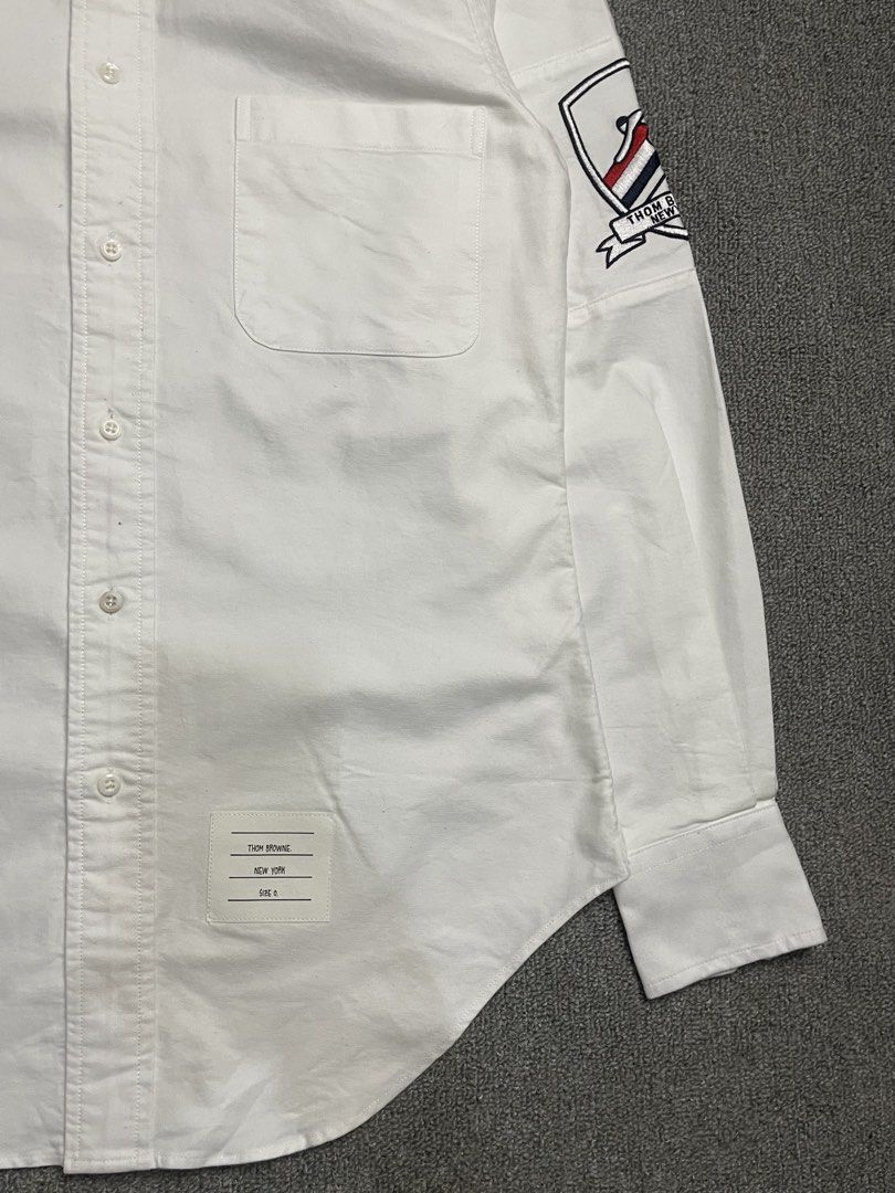 Thom Browne New York White Button-Down Shirt with Patch (Category: Tshirts & Polo Shirts ) located in Quezon City. Submitted by cozy_thrifting (Listing ID 1462595234, Image 3). Description: - Classic white button-down shirt - Brand: Thom Browne - Signature sleeve patch detail - Button collar - Chest pocket - Tagged size: 1 - Ideal for smart casual outfits 18.5 Width 28 Length 23.5 Sleeves .