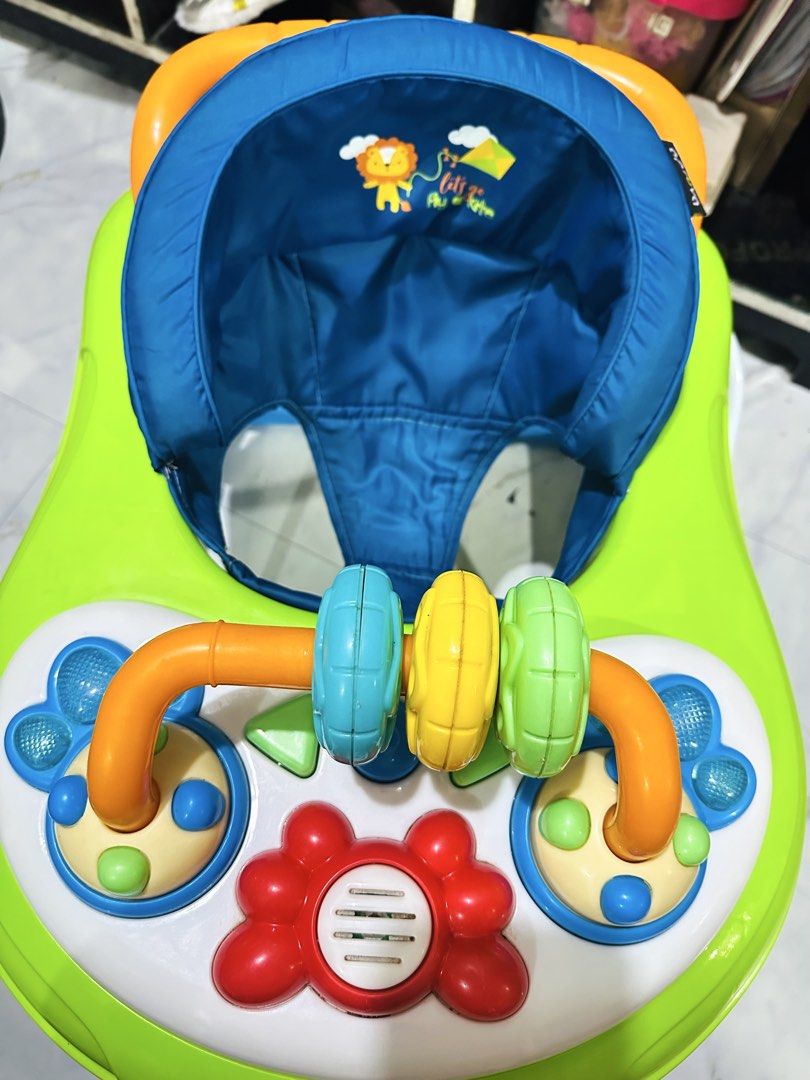Apruva Baby Walker with Toys (Category: Infant Playtime) located in Manila. Submitted by allysa023025488 (Listing ID 1462820768, Image 3). Description: Aprica baby walker in green and blue. Has a toy bar with spinning rings and buttons. Seat is blue with a lion print. Some wear and tear on the metal legs, as shown in photos. Still functional for little ones learning to walk..