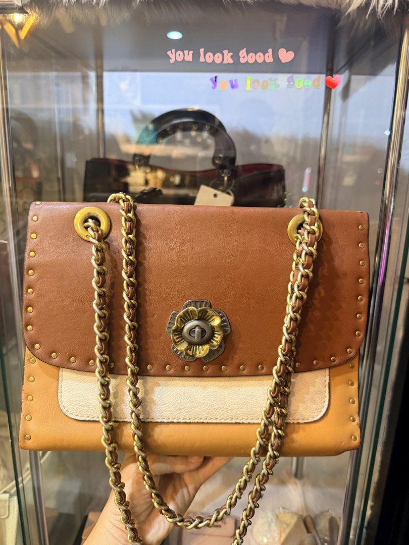Authentic Coach Brown Leather Studded Chain Shoulder Bag (Category: Luxury Bags & Wallets) located in Dumaguete. Submitted by lovebags.ph (Listing ID 1462825780, Image 2). Description: - Stylish brown and cream leather shoulder bag - Elegant gold chain strap - Eye-catching studded details all around - Unique flower clasp closure - Practical interior with multiple compartments - Versatile for everyday wear or evening events.