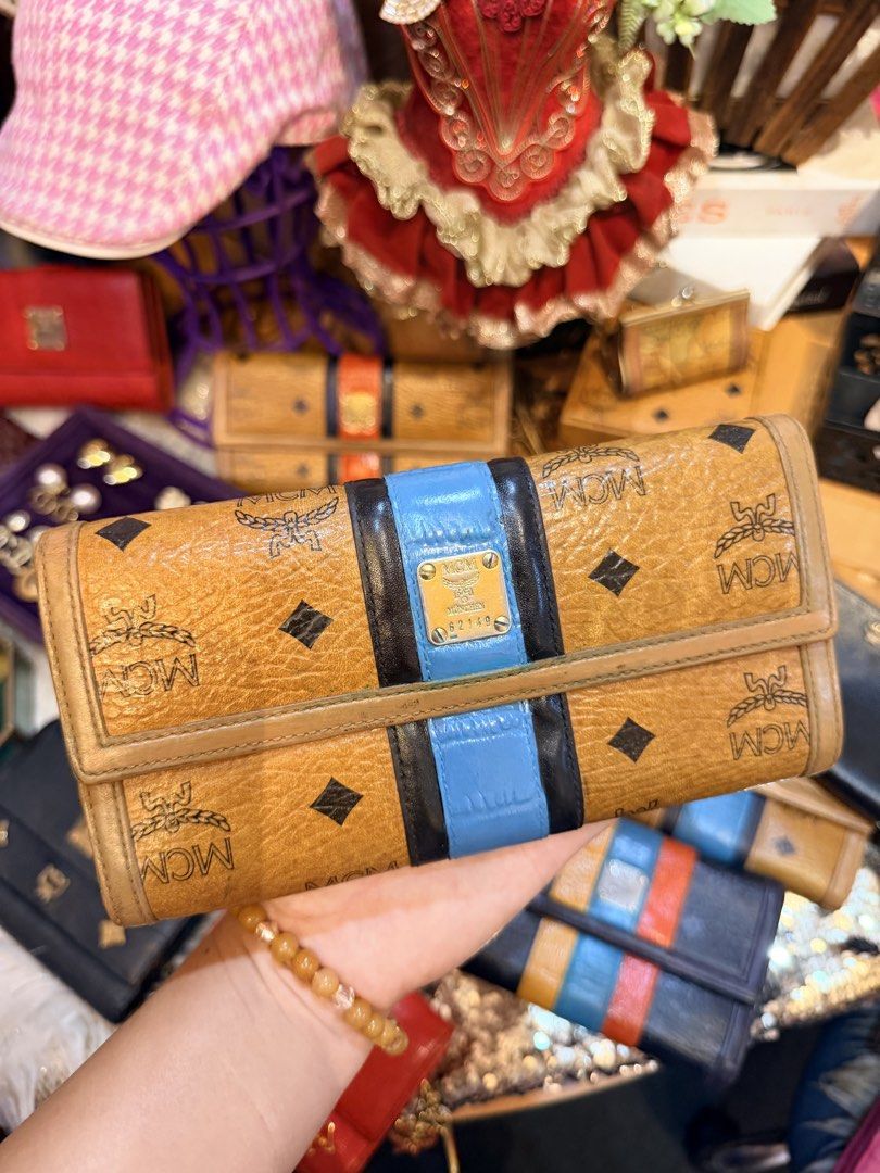 Authentic MCM Visetos Trifold Wallet Cognac Blue Black (Category: Luxury Bags & Wallets) located in Dumaguete. Submitted by lovebags.ph (Listing ID 1462826031, Image 2). Description: - Classic MCM trifold wallet - Signature Visetos print - Brown, blue, and black stripe detail on front - Tan leather interior - Multiple card slots and ID windows - Snap closure - Shows some signs of wear consistent with regular use.