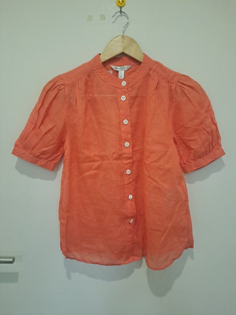 Banana Republic linen fabric (Category: Blouses) located in Manila. Submitted by joanbalde39643 (Listing ID 1462798309, Image 1). Description: This is a women's Banana Republic short-sleeve button-up blouse crafted from 100% ramie or linen. It features a vibrant coral orange tone, a classic band/mandarin collar, white contrast buttons down the front, and feminine puff sleeves..