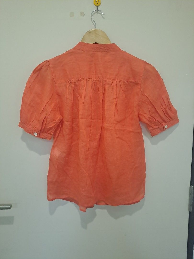 Banana Republic linen fabric (Category: Blouses) located in Manila. Submitted by joanbalde39643 (Listing ID 1462798309, Image 3). Description: This is a women's Banana Republic short-sleeve button-up blouse crafted from 100% ramie or linen. It features a vibrant coral orange tone, a classic band/mandarin collar, white contrast buttons down the front, and feminine puff sleeves..