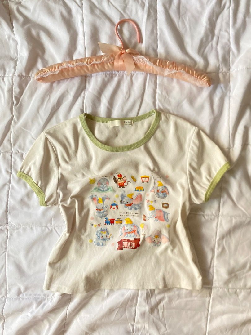 Disney Dumbo Graphic T-shirt (Category: Shirts) located in Laoag. Submitted by shop.kawes (Listing ID 1462688305, Image 1). Description: - Adorable cream t-shirt featuring a Dumbo circus graphic print. - Accented with green trim on the neckline and sleeves. - Likely a size small (based on tag). - Ideal for casual wear and Disney enthusiasts. #babytee #cutesy.