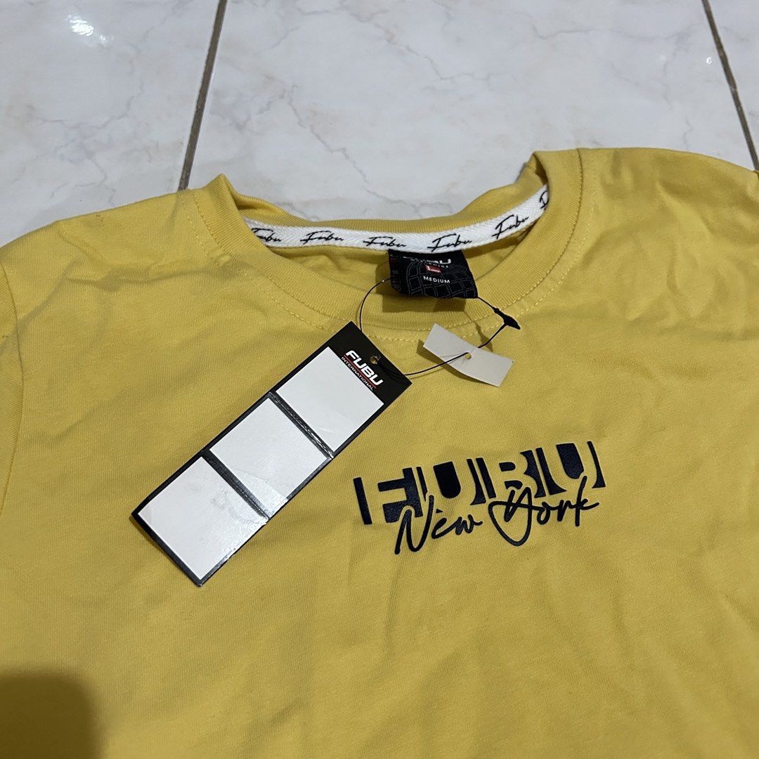 FUBU New York Yellow T-shirt (Category: Shirts) located in Bacoor. Submitted by kyespreloved (Listing ID 1462829087, Image 2). Description: - Yellow FUBU t-shirt - FUBU New York graphic on front - FUBU Worldwide tag - Size: Medium - Original tags attached - Classic streetwear style - Perfect for casual wear.